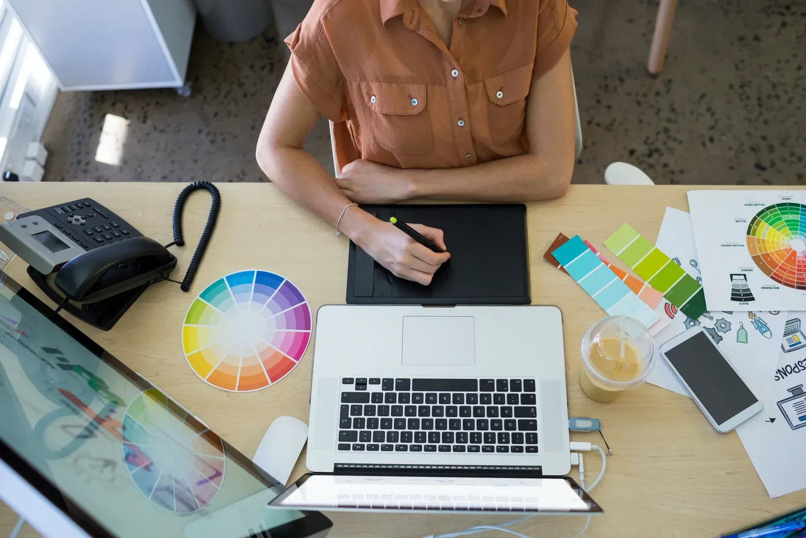 Overhead view of a designer exploring options with a colour wheel, swatch fans and a laptop.