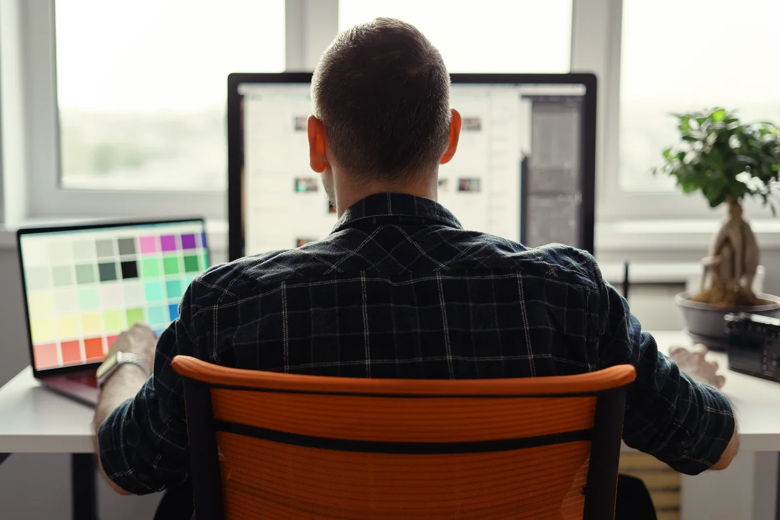 A person at a home desk reviewing a colour palette spread across two screens.